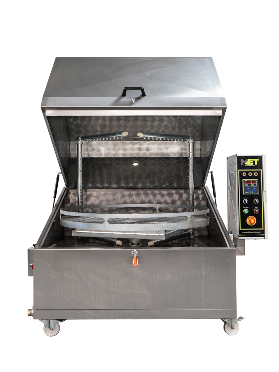 Open industrial parts washer with control panel and rotating spray arms inside for cleaning large metal parts.